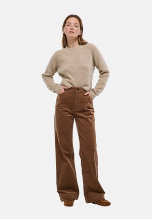 Pull en tricot beige à manches longues associé à un pantalon large en velours côtelé brun taille haute. Une chaussure décontractée complète la tenue.