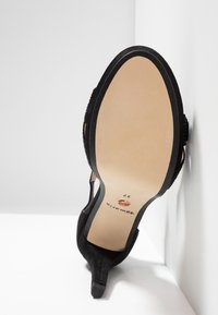 Chaussure à talon haut en daim noir reposant sur son talon, présentant une semelle beige propre avec la taille 37 et l'inscription de la marque.