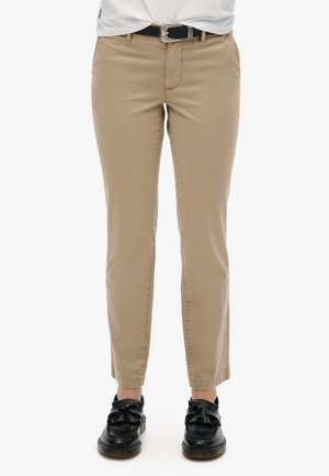 Chinos beige con un corte slim, que presentan una textura suave, bolsillos frontales y un cinturón negro con una hebilla decorativa.