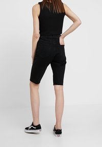 Zwarte denim shorts met een hoge taille, een verwoeste zoom en achterzakken, gecombineerd met zwarte sneakers en een mouwloos topje.