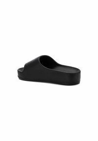 Sandalia de slide negra con una textura suave y mate. Presenta una punta abierta y un diseño curvado en la parte superior, descansando sobre una suela gruesa y plana.