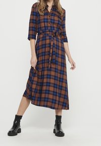Hnědá kostkovaná midi šaty s modrými akcenty, zapínání na knoflíky vpředu, tříčtvrteční rukávy a odpovídající pásek, s volným lemem.