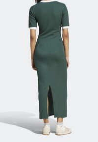 Žebrované zelené šaty s krátkými rukávy a bílým lemem, se bočním rozparkem. V kombinaci s bílými teniskami a pruhovanými ponožkami.