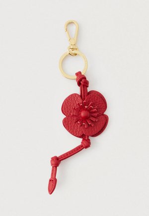 Punainen nahkakukkakranssi avaimenperä, jossa on kultainen metallirengas ja koukku, sekä solmitta vyö yksityiskohtana vaaleaa taustaa vasten.