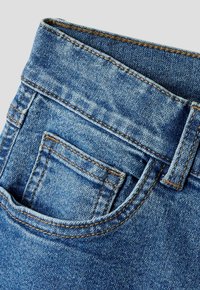 Nærbilde av blå denimjeans som viser den øvre delen med beltehempe, midjebånd og forlommer med myntlomme.