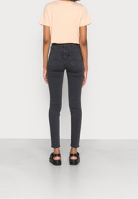 Jeans negros ajustados con cintura alta, detalles de costura sutiles y una textura suave, combinados con una blusa de manga corta en tono melocotón claro.