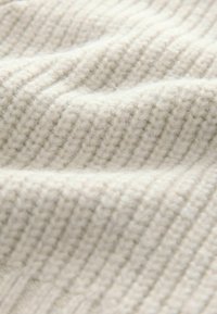 Lys cremefarvet strikket stof med ribbet tekstur og bløde, fluffy fibre, hvilket skaber et hyggeligt og varmt udseende.