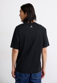Sort bomulds T-shirt med korte ærmer og rund hals. Har et hvidt Jordan-logo på den øverste del af ryggen. Casual pasform og glat tekstur.