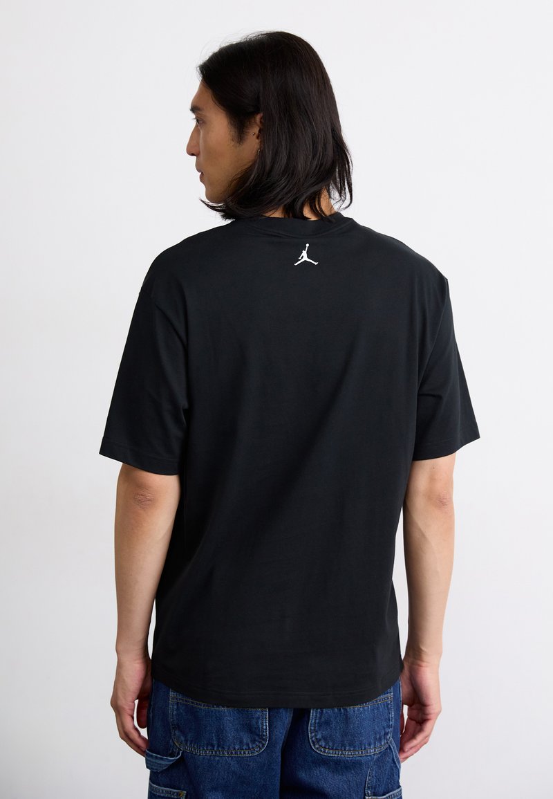 Schwarzes Baumwoll-T-Shirt mit kurzen Ärmeln und Rundhalsausschnitt. Verfügt über ein weißes Jordan-Logo auf dem oberen Rücken. Lässige Passform und glatte Textur.
