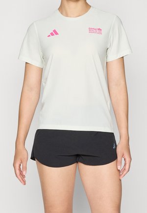 Persona che indossa una maglietta bianca BMW Berlin Marathon con loghi rosa e pantaloncini da corsa Adidas neri.