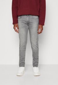 Vaqueros de mezclilla gris ajustados, con una cintura de altura media, cinco bolsillos y un ligero desgastado. Combinados con zapatillas blancas y un sudadera burdeos.