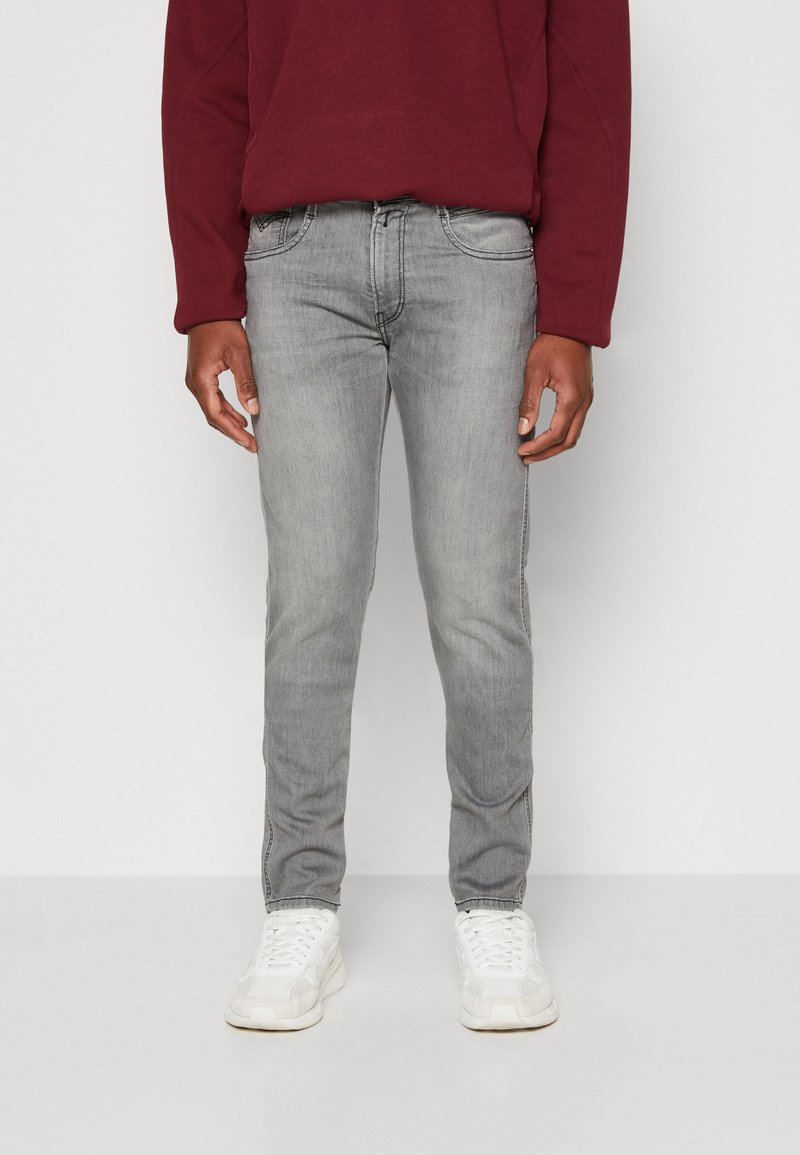 Vaqueros de mezclilla gris ajustados, con una cintura de altura media, cinco bolsillos y un ligero desgastado. Combinados con zapatillas blancas y un sudadera burdeos.