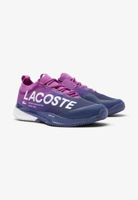 Scarpe da ginnastica viola e blu navy con tomaia in rete, marchio "LACOSTE" bianco e suola in gomma testurizzata progettata per le prestazioni sportive.