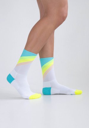 Socken mit weißem Grund, die diagonale Bänder in Türkis, Neon-Gelb und Hellrosa aufweisen. Die Zehen sind leuchtend gelb und haben ein strukturiertes Strickmuster.