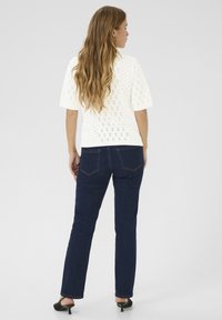Haut en tricot blanc à manches courtes et texture à motif en losange, associé à un jean ajusté bleu marine et des sandales à talons noires.
