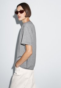 Grå bomulds t-shirt med afslappet fit, kortærmede, og rund halsudskæring, parret med hvide brede bukser og brune solbriller.