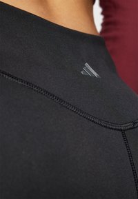 Svart idrettsgenser med en tettsittende design, med en subtil logo og teksturerte sømmer, som fremhever elastisk og fukttransporterende materiale.