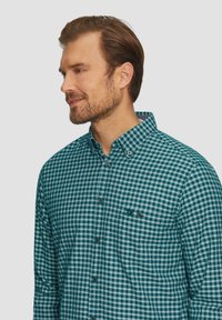 Gekruiste blouse in groen en wit. Katoenen stof met een zachte textuur. Heeft een puntige kraag en een logo-opdruk op de borst.