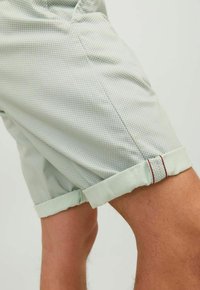 Lichtgroene geruite shorts, gemaakt van zachte stof, met opgerolde cuffs en rode stikselaccenten. Close-up van de zijkant.