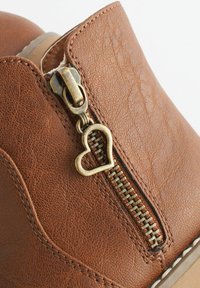 Brązowy ankle boot z sztucznej skóry z złotym zamkiem błyskawicznym z sercowym uchwytem, teksturowaną powierzchnią i kontrastowym przeszyciem.