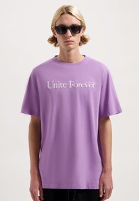 Paarse korte mouwen T-shirt van katoen, met de tekst "Unite Forever" in witte borduursel over de borst. Casual pasvorm.