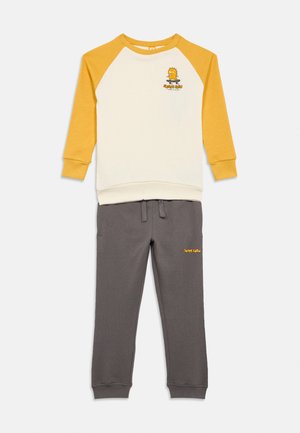 Tweedelige outfit met een crèmekleurig en geel langemouwen top met cartoonprint en grijze broek met gele geborduurde tekst. Katoenmengsel stof.