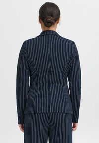 Blazer bleu marine à rayures, avec une coupe ajustée, revers cranté et manches longues ; présente des rayures verticales blanches. Vu de dos.