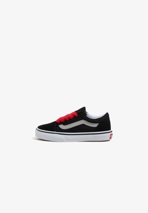 Zapatilla negra de caña baja con franja blanca en forma de ola, cordones rojos, suela blanca y lengüeta roja en el talón sobre fondo blanco.