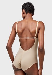 Bodysuit beige con escote en la espalda, tirantes ajustables y textura suave. Presenta una costura fruncida en la parte posterior y acentos de hardware transparente.