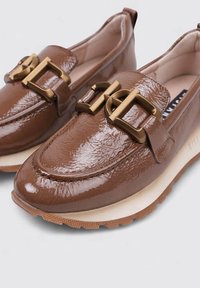Mocasines de charol marrón con puntera redondeada, con herrajes en tono dorado y superficie texturizada. Suela de goma color crema.