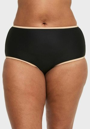 Middenstuk van een persoon die een zwart, hoog uitgesneden ondergoed met beige rand draagt, staand tegen een effen lichte achtergrond.