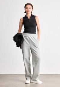 Czarny bezrękawnik z zamkiem przy kołnierzu, w zestawieniu z jasnoszarymi spodniami dresowymi z elastycznym pasem i bocznymi kieszeniami. Białe sneakersy dopełniają stylizację.