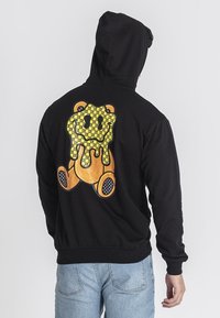 Felpa nera con cappuccio caratterizzata da una grande grafica di un orso colorato sul retro con un motivo a scacchi. Vestibilità regolare, tessuto morbido, tasca a marsupio.
