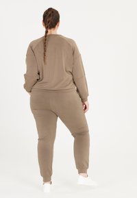 Brunt loungewear-set tillverkat av mjukt tyg; inkluderar en långärmad topp och tapered byxor med elastiska muddar. Enkel design, avslappnad passform.