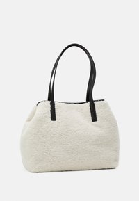 Sac fourre-tout en fausse fourrure couleur crème avec des accents en cuir noir. Dispose de deux longues poignées et d'une surface douce et texturée.