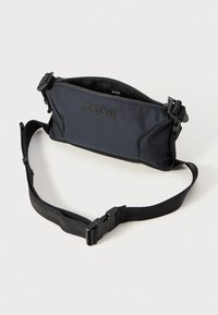 Crni tkaninski fanny pack s zatvaračem na munje, podesivim remenom i reljefnim logotipom "BOSS". Glatka tekstura i pojednostavljen dizajn.