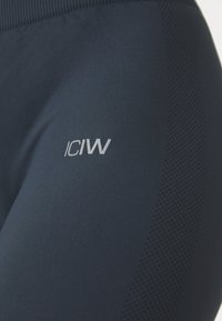 Námořnické modré sportovní legíny s texturovaným panýlkem, vyšitým logem ve světlejší barvě a hladkým, elastickým materiálem.
