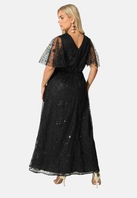 Mustatylli mekko, jossa on kukkakirjontaa ja paljetteja, lyhyet liehuvat hihat ja V-muotoinen selkäosa. Yhdistetty vaaleanvärisiin korkokenkiin.