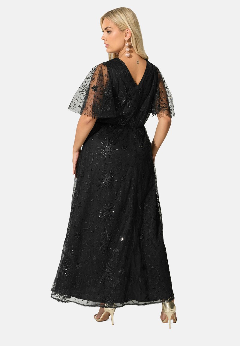 Mustatylli mekko, jossa on kukkakirjontaa ja paljetteja, lyhyet liehuvat hihat ja V-muotoinen selkäosa. Yhdistetty vaaleanvärisiin korkokenkiin.