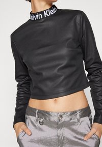 Czarna krótka bluzka z długim rękawem z prążkowanym dekoltem z logo "Calvin Klein". Gładka tekstura, w połączeniu z błyszczącymi srebrnymi spodniami.
