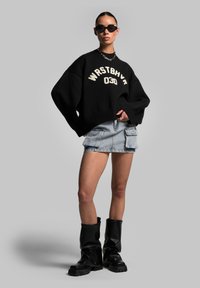 Black knitted sweater with white lettering, paired with a denim mini skirt featuring cargo pockets, and black knee-high chunky boots.