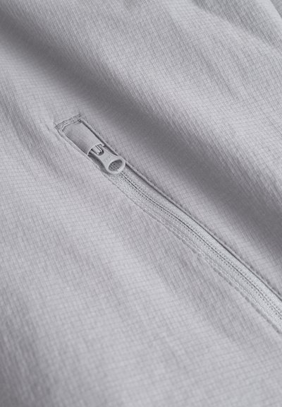Tissu gris clair avec une fermeture éclair dotée d'une tirette rectangulaire, surface texturée avec un motif en grille, et coutures précises le long des bords.