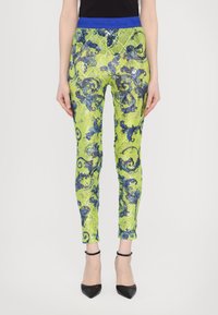 Leggings verdes con lentejuelas que presentan una cinturilla azul, adornados con un intrincado patrón floral azul. Diseño ajustado con pierna entallada.