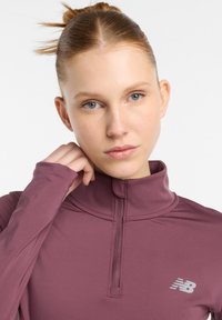 Bordeaux sportieve quarter-zip top gemaakt van gladde, rekbare stof. Kenmerkend is de hoge kraag en een klein logo aan de linkerzijde.