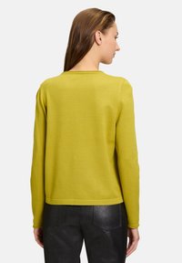 Maglione giallo lavorato a maglia con scollo rotondo, maniche lunghe e vestibilità corta. Texture liscia e dettagli di design minimi sul retro.