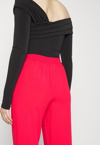 Svart avskuren topp med draperad textur kombineras med klarröda, elastiska vida byxor. Slätt tyg och avslappnad passform.