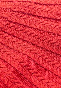 Röd stickad tyg med en strukturerad kabelmönster som har diagonala linjer och upphöjda stygn, vilket skapar djup och visuell intresse.