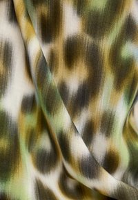 Textil mit einer weichen, glatten Textur, die eine Mischung aus Grün, Braun und Creme in einem fließenden, abstrakten Muster aufweist.