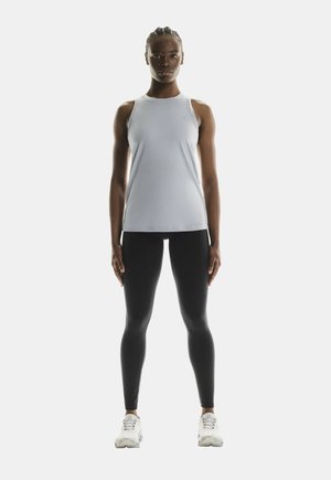 Light gray, sleeveless athletic top with subtle logo; paired with black, form-fitting leggings and white sneakers. Simple design, streamlined look.
