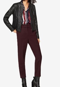 Mustat nahkatakki, jossa on tiukka muotoilu, yhdistettynä viininpunaisiin korkeavyötäröisiin housuihin ja moniväriseen raidalliseen paitaan. Kiiltävät nilkkurit.